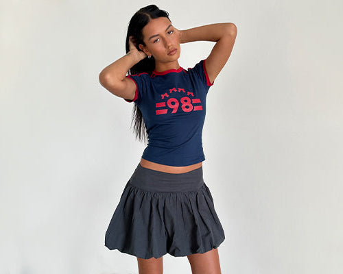 Abbildung von Salda Tee in Navy mit roter Adrenalin-Bindung und '98'-Emblem und Kiyowo Puffball Mini Rock in Charcoal Grey